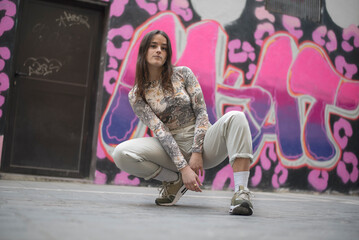 a modern young dancer poses in front of a street graffiti backdrop
