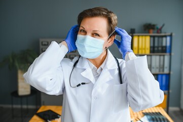 Portrait of a female doctor wearing face mask and holding her patient chart on digital tablet while standing at the hospital.