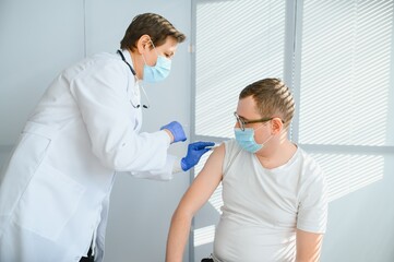 Obraz premium Female doctor making injecting using syringe to male patient in hospital. Senior man taking injection for flu in clinic. Female doctor vaccinating a man.