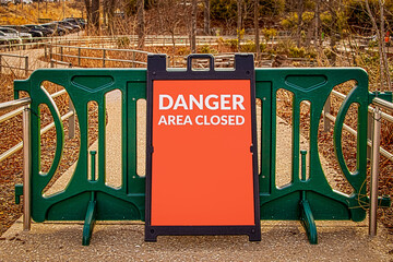 Outdoor green modular gate on public pebble and concrete sidewalk with sandwich sign reading DANGER...