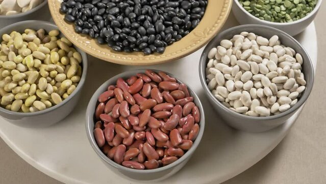 Variety beans in bowls rotating closeup. Legumes - Mayocoba, black, kidney red and white, lima beans, peas. Healthy diet, vegan protein source, plant-based food concept.