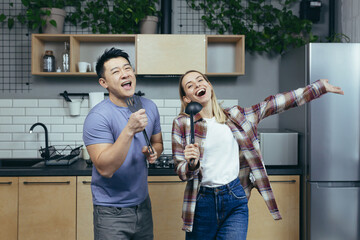 Happy young Asian man and woman couple singing and dancing together in the kitchen, having fun together, family in love
