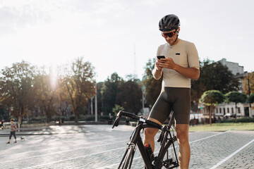 Male athlete sitting on bike and using smartphone
