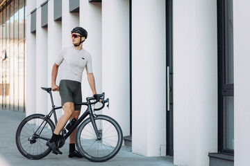 Fototapeta premium Man in activewear and helmet standing on street with bike