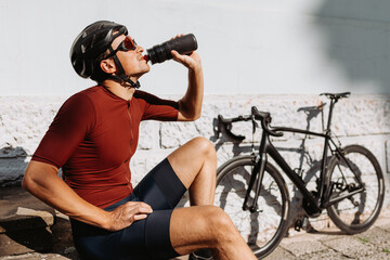 Plakat Cyclist in sportswear drinking water after ride outdoors