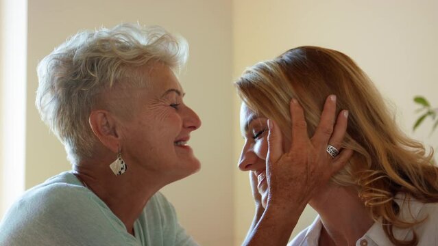 Happy senior mother kissing her adult daughter on forehead.