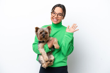 Young hispanic woman holding a dog isolated on white background saluting with hand with happy...