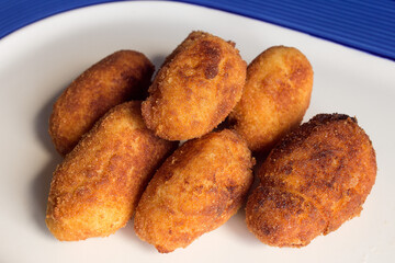 A group of fried golden croquettes on a plate decorated with blue lines. Textures and food.