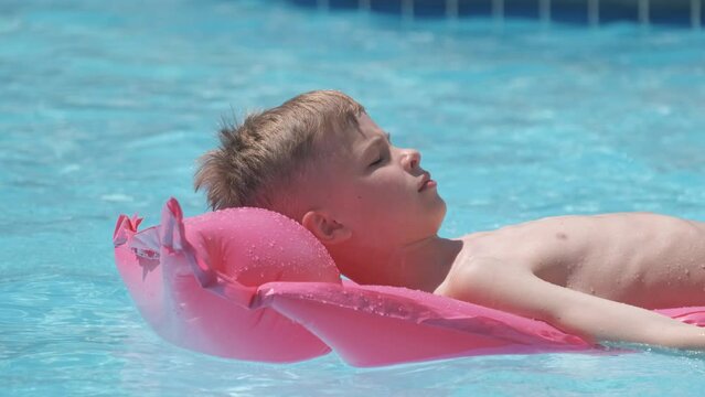 Young child boy relaxing on summer sun swimming on inflatable air mattress in swimming pool during tropical vacations. Summertime activities concept