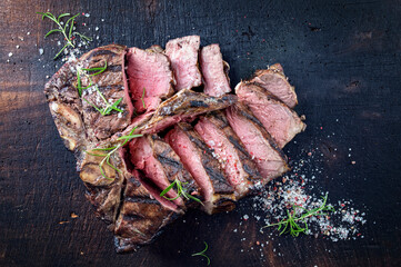 Traditional dry aged barbecue angus porterhouse beef steak sliced and served with salt and pepper as top view on a old charred wooden board