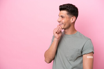 Young caucasian man wearing band-aids isolated on pink background thinking an idea and looking side