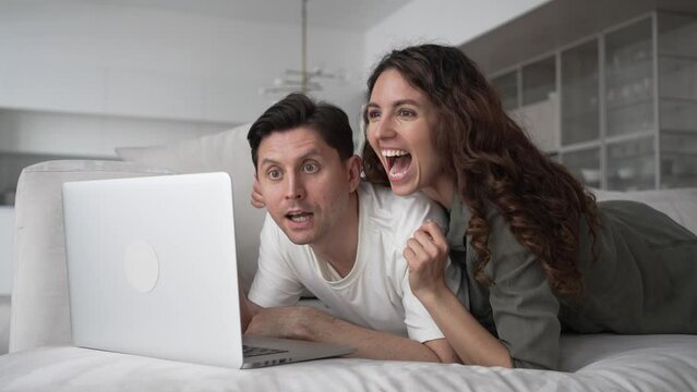 Exalted brunette wife and excited short-haired husband do online shopping for new apartment looking for discounts on sofa in living room