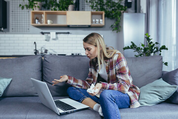 Obraz premium Young beautiful woman at home alone, uses laptop for online consultation with a psychotherapist, makes a video call to the support line, sits on the couch and cries
