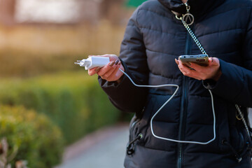 Charger in the female hand of a tourist with a discharged smartphone lifestyle outdoors. Selective...