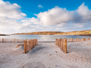 Entrance to beautiful sandy beach through wooden fence to protect and preserve dune. Stunning Dog's bay, county Galway, Ireland. Blue cloudy sky. Hidden travel gem in Connemara. Care about nature