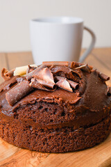 Traditional round chocolate cake with white and dark chocolate shavings or chips on top and cup of tea in the background. Bakery product on a wooden board and table. Birthday cake.