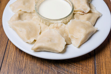 Serving of polish dumplings with small bowl of sour cream, close up. Traditional simple food.
