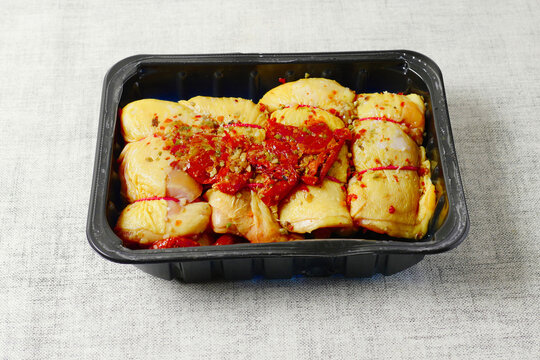 Rolled corn fed chicken thigs with herbs on a black plastic tray. Poultry product.