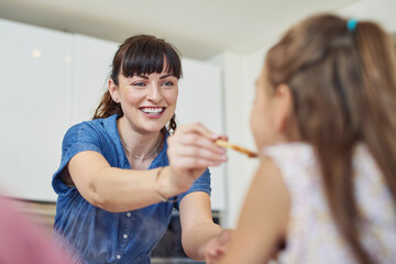 I made your favourite. Shot of a mother giving her daughter a taste of the meal that shes cooking at home.