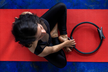 Top view of Latin American woman (38) doing toning pilates exercise with exercise ring on red...