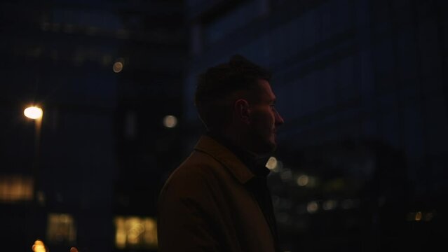 View camera move around brunette man businessman guy in causal coat tourist standing in city outdoors looking at urban buildings enjoying sunset sunlight at night.