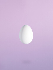 Minimal Easter composition with levitating white egg against pastel purple background.