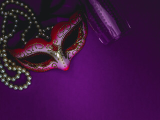 A masquerade mask, white pearl beads and an empty champagne glass on a purple-lilac background.