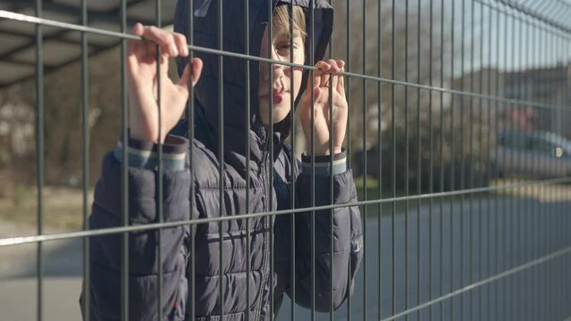 Boy child refugee behind a metal fence. Social problem of war migrants.