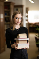 a female student standing in the library holding many books in her hands