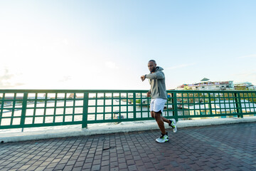  Confidence African man in sportswear and smart watch jogging exercise on the bridge in the city at summer sunset. Strong male athlete enjoy outdoor activity lifestyle sport training running workout. 