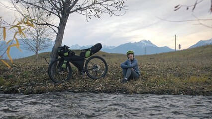 Obraz premium The woman travel on mixed terrain cycle touring with bikepacking. The traveler journey with bicycle bags. Sportswear in green black colors. The trip in magical autumn forest, river stream.
