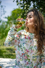 Fototapeta premium Portrait of beautiful woman posing lying on plaid at summer garden park. A book, fruit, a bag and a watermelon are next to each other.