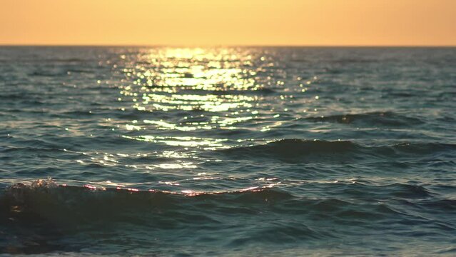 Sea, ocean surface with small waves and sunrise, sunset beams reflecting on the surface