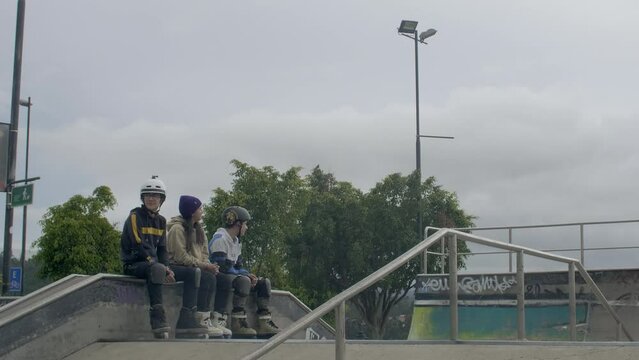 three males jump and rail at skatepark while three other people watch them