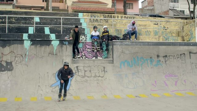 three males skate at skatepark while two young boys watch