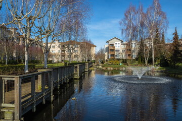 Fototapeta na wymiar Residential District in Richmond City with pond and fountain, green grass bushes and trees in the territory of residential complex, Vanсouver, British Columbia 