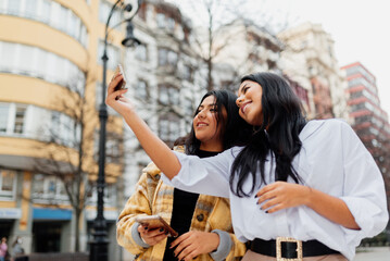 Fototapeta na wymiar two young latin women and sisters taking a picture with their smartphone. Women making a selfie on the street during a trip.
