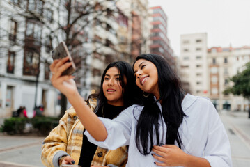 two young latin women and sisters taking a picture with their smartphone. Women making a selfie on the street during a trip.
