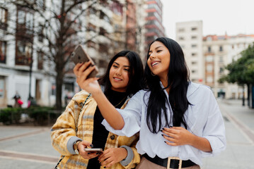 Two young and cheerful Latin women take a picture with their mobile phone while tourism in a city during a trip. sisters having a good time together