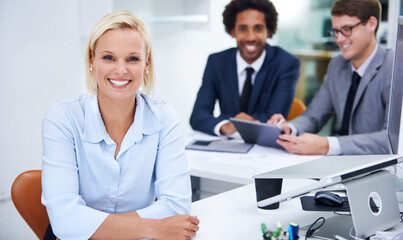 Happy to be pursuing my career. Portrait of a confident businesswoman sitting with her colleagues in the background.