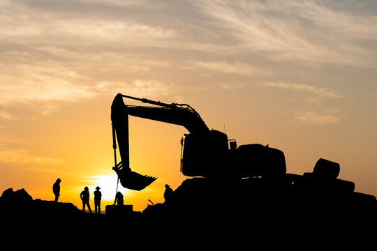 Silhouette of Foreman and workers team at construction site, Road construction worker and excavator with blurred sunset background