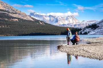 Fototapeta na wymiar Playful children sitting at a lakeside preparing to skip rocks near Banff Canada in the Rocky Mountains of North America