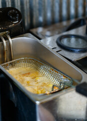 Closeup shot of delicious tasty yummy fresh cooked fast junk food snacks golden fatty french fries and greasy chicken nuggets in stainless steel metal cooking basket in automatic oil frying machine