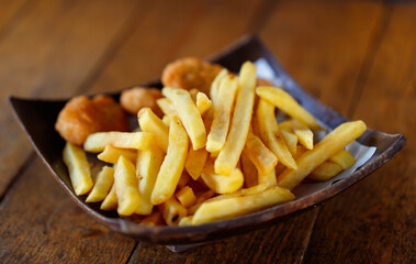 Closeup shot delicious tasty yummy fast junk food snack appetizer pan frying home cooking straight cut french fries and golden crispy chicken meat nuggets in wooden plate placed on wood table counter