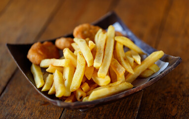 Closeup shot delicious tasty yummy fast junk food snack appetizer pan frying home cooking straight cut french fries and golden crispy chicken meat nuggets in wooden plate placed on wood table counter