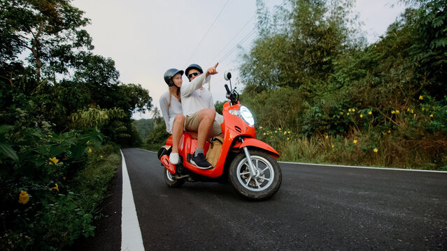 Scooter road trip. Love couple on red motorbike in white clothes on forest road trail. Just married woman and man kiss, hugs, sit on motorbike. Wedding, honeymoon. Motorcycle rent. Safety helmet.