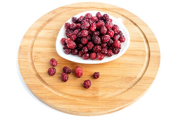 On a light kitchen board, a white plate with dried healthy cranberries. White background.