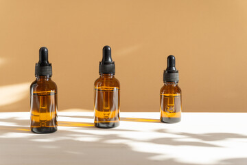 Three mock-ups of unmarked glass bottles, amber in color with dropper lid on beige background with...
