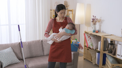 Korean mom having housework is trying to be patient while putting her baby in arms to sleep with...