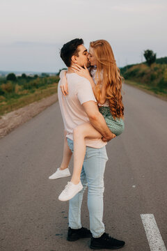 Man holding his girlfriend in his arms and kissing in the middle of the road outside the city. Summer vacation. Beautiful female person.
